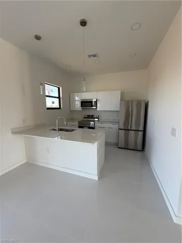 Kitchen featuring white cabinetry, stainless steel appliances, a peninsula, pendant lighting, and modern cabinets