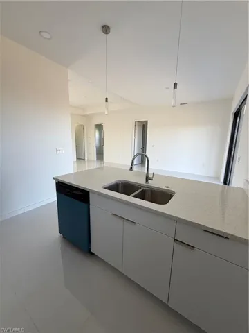 Kitchen featuring light stone countertops, dishwashing machine, white cabinets, decorative light fixtures, and modern cabinets