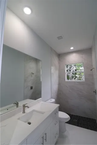 Bathroom featuring vanity, tiled shower, toilet, and tile patterned flooring