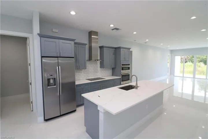 Kitchen with tasteful backsplash, stainless steel appliances, sink, light tile patterned floors, and wall chimney exhaust hood