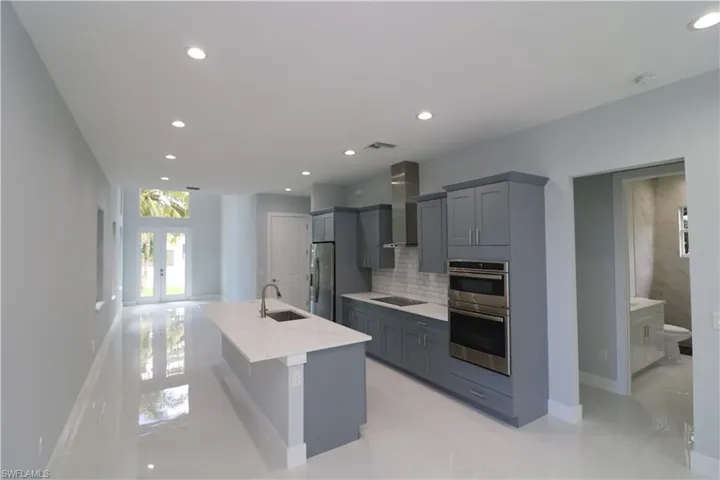 Kitchen featuring appliances with stainless steel finishes, a center island with sink, wall chimney range hood, light stone counters, and light tile patterned flooring