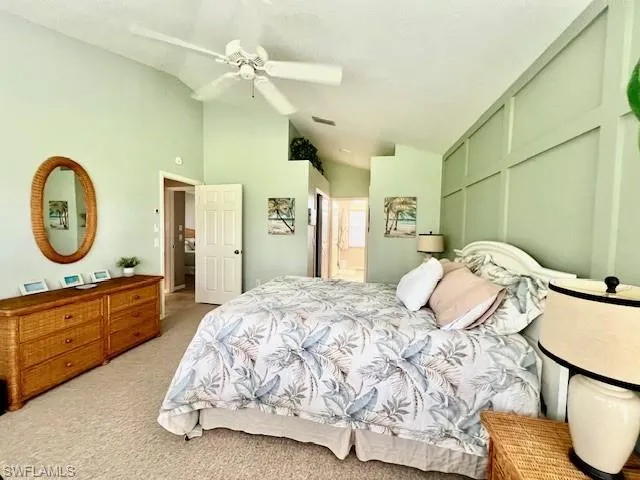 Bedroom with lofted ceiling, light colored carpet, ensuite bathroom, and ceiling fan