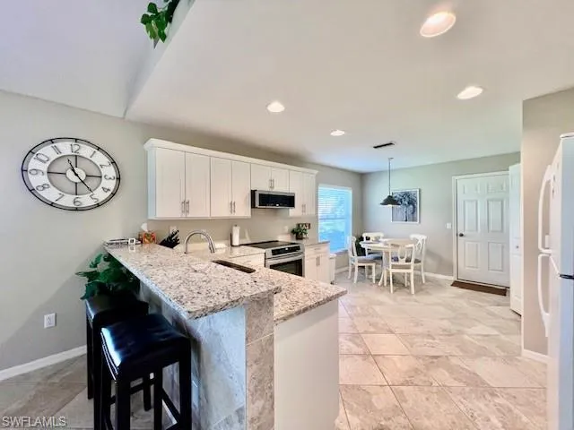 Kitchen featuring white cabinets, appliances with stainless steel finishes, light stone counters, a sink, and a peninsula
