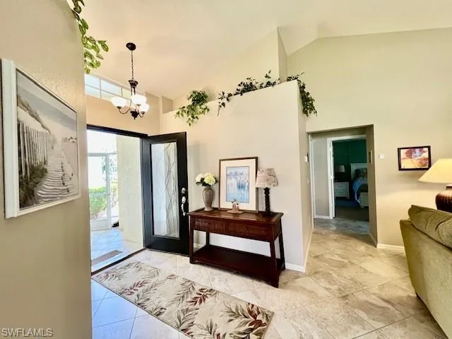 Tiled foyer with high vaulted ceiling, a notable chandelier, and baseboards