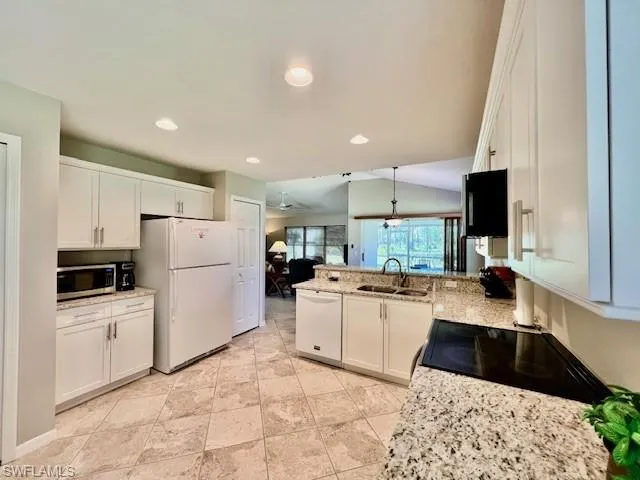 Kitchen with a peninsula, white appliances, recessed lighting, white cabinets, and a sink