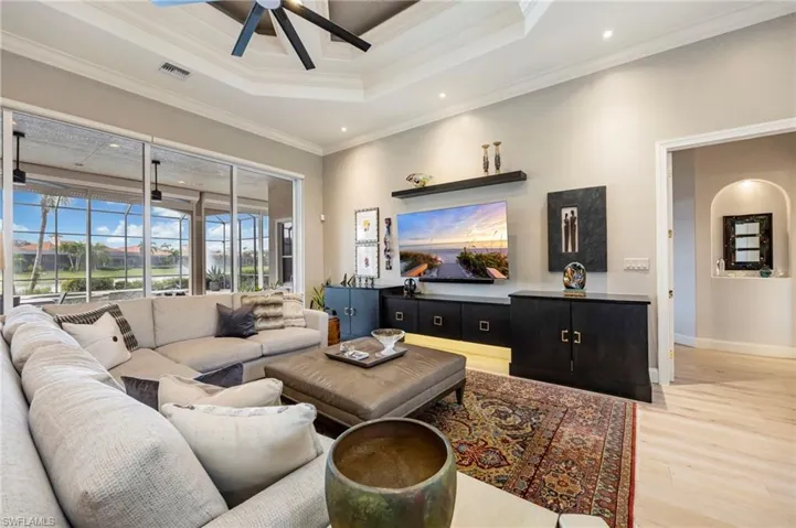 Living area featuring light wood finished floors, ceiling fan, ornamental molding, a tray ceiling, and recessed lighting
