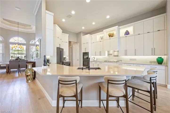 Kitchen with white cabinetry, backsplash, light wood-type flooring, a kitchen breakfast bar, and a peninsula