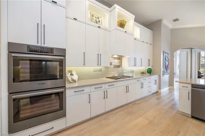 Kitchen with stainless steel appliances, arched walkways, light wood-style flooring, white cabinets, and ornamental molding