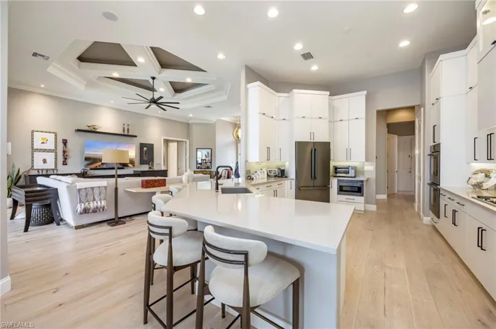 Kitchen with a peninsula, a kitchen bar, coffered ceiling, light wood-style floors, and appliances with stainless steel finishes