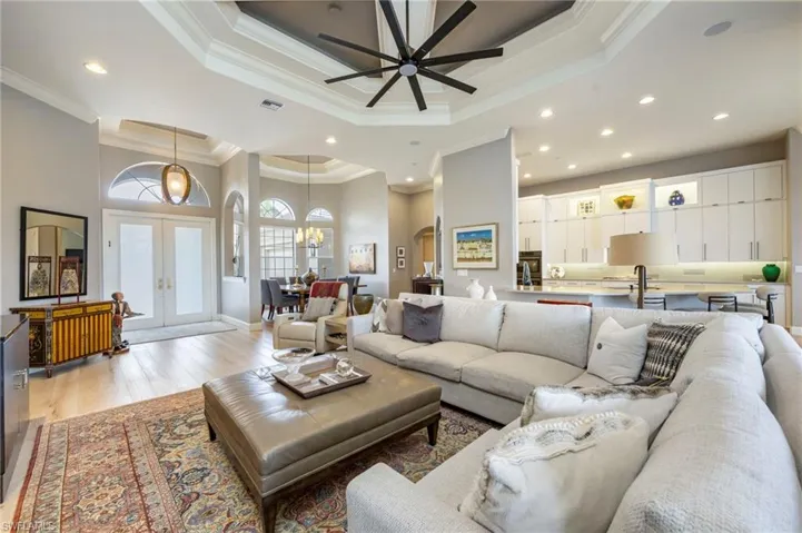 Living area featuring french doors, light wood-style floors, a tray ceiling, a high ceiling, and recessed lighting