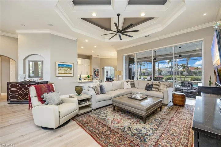 Living room featuring arched walkways, coffered ceiling, a high ceiling, crown molding, and light wood-style flooring