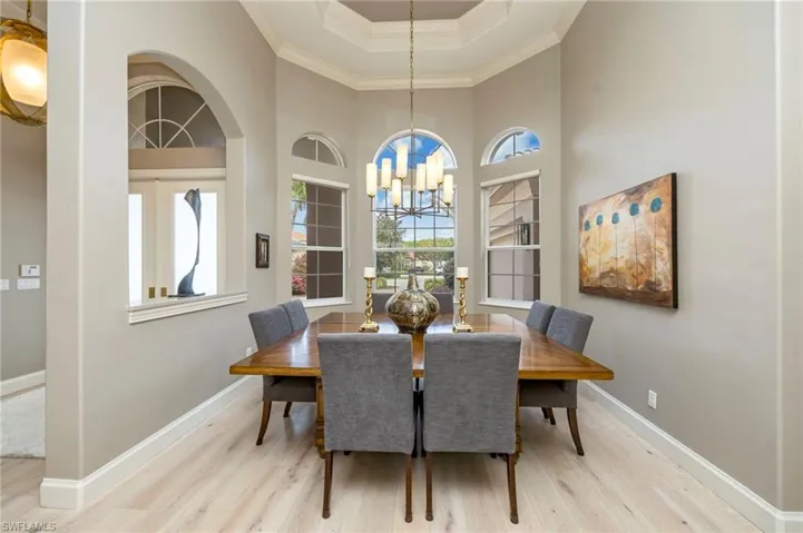 Dining area featuring crown molding, light wood finished floors, a raised ceiling, a chandelier, and a towering ceiling