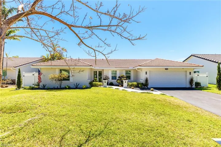 View of front of house with a front lawn, fence, a tiled roof, driveway, and an attached garage