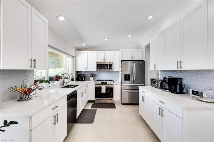 Kitchen with lofted ceiling, light tile patterned flooring, white cabinets, stainless steel appliances, and a sink