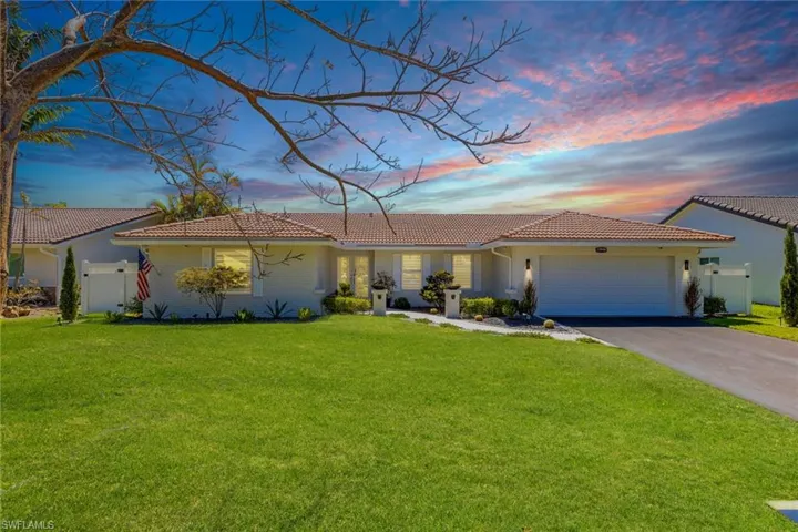 View of front of home with a lawn, aphalt driveway, fence, a garage, and a tiled roof
