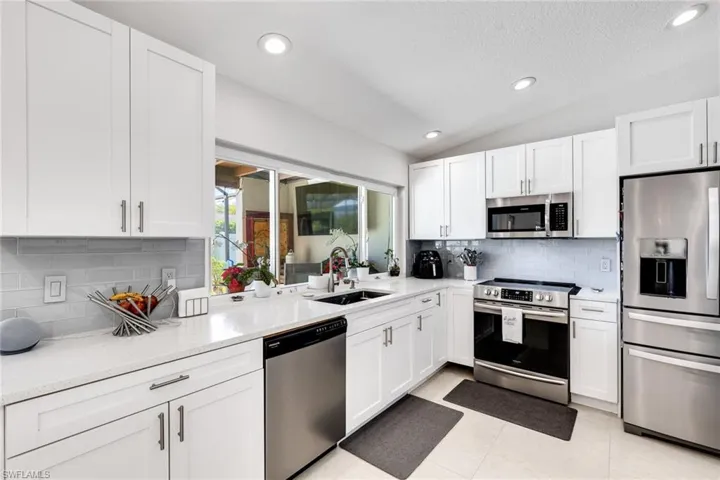 Kitchen featuring lofted ceiling, a sink, light countertops, appliances with stainless steel finishes, and white cabinetry
