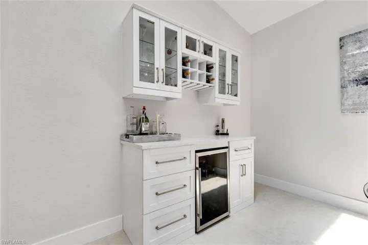 Bar with a bar, light tile patterned flooring, beverage cooler, and baseboards