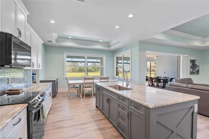 Kitchen featuring a raised ceiling, black appliances, light stone countertops, open floor plan, and recessed lighting