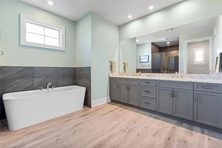 Full bathroom with a shower stall, double vanity, a soaking tub, light wood-style flooring, and tile walls