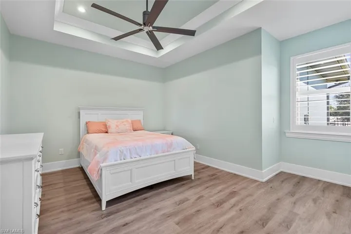 Bedroom featuring a tray ceiling, light wood-style floors, and ceiling fan
