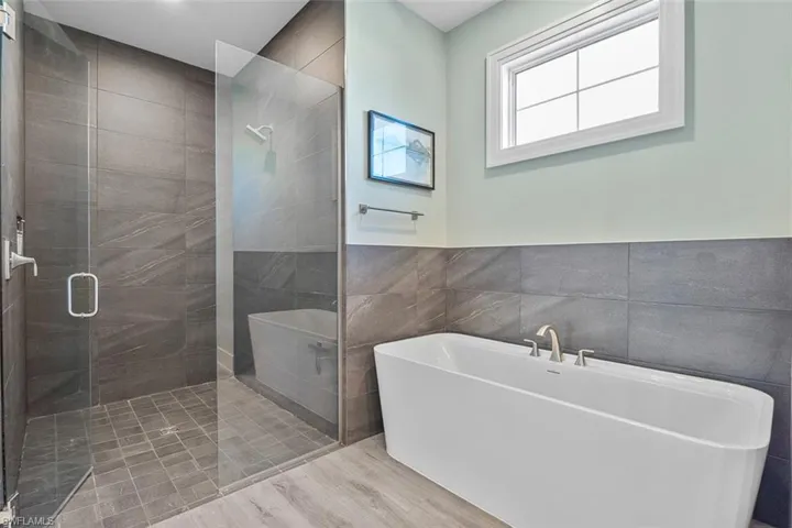 Bathroom with tile walls, a soaking tub, a stall shower, and wood finished floors