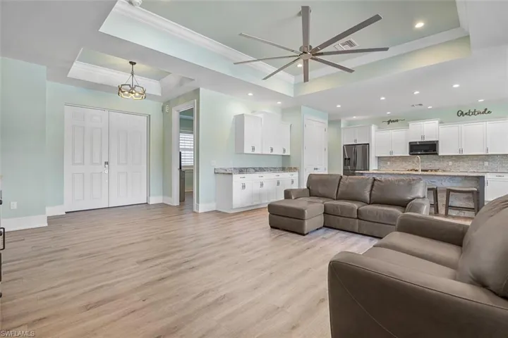 Living room with a raised ceiling, light wood finished floors, crown molding, ceiling fan, and recessed lighting