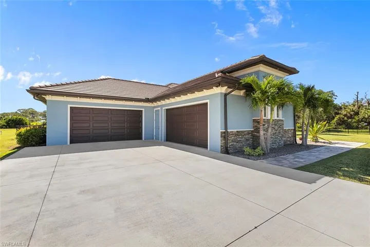 View of side of property featuring concrete driveway, an attached garage, stucco siding, stone siding, and a tiled roof