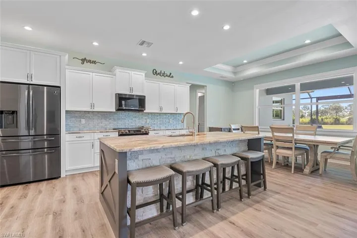 Kitchen with stainless steel appliances, backsplash, a raised ceiling, light stone counters, and light wood-style flooring
