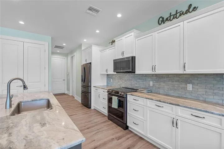 Kitchen with appliances with stainless steel finishes, white cabinetry, light stone counters, and recessed lighting