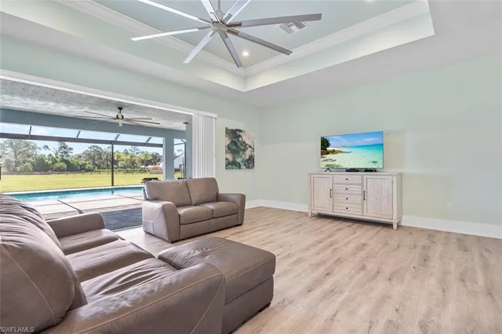 Living area with a tray ceiling, a sunroom, crown molding, light wood-style flooring, and a ceiling fan