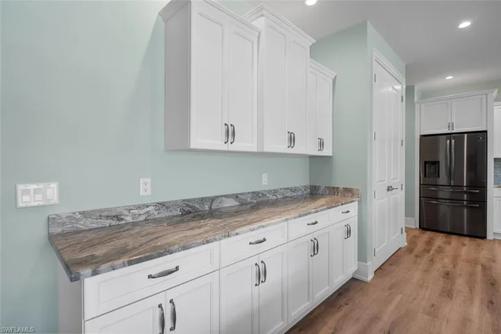 Kitchen with white cabinetry, stainless steel refrigerator with ice dispenser, light wood-style flooring, dark stone countertops, and recessed lighting