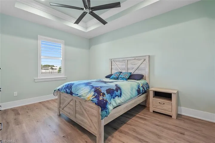 Bedroom with a raised ceiling, ornamental molding, a ceiling fan, and light wood-type flooring