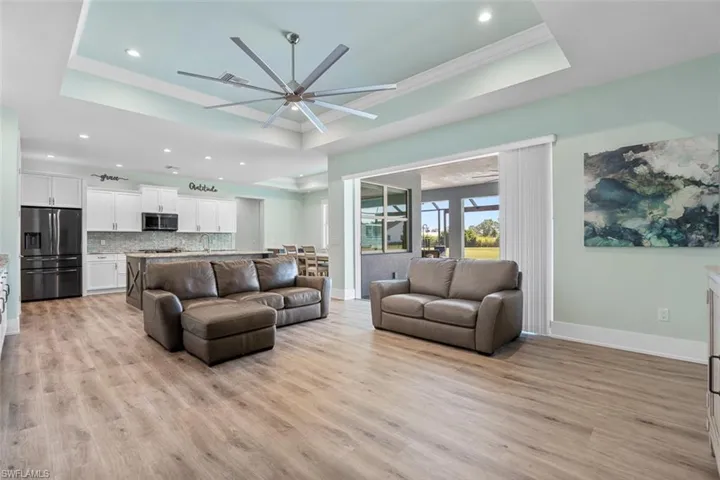 Living room featuring a raised ceiling, light wood-style floors, recessed lighting, ornamental molding, and ceiling fan