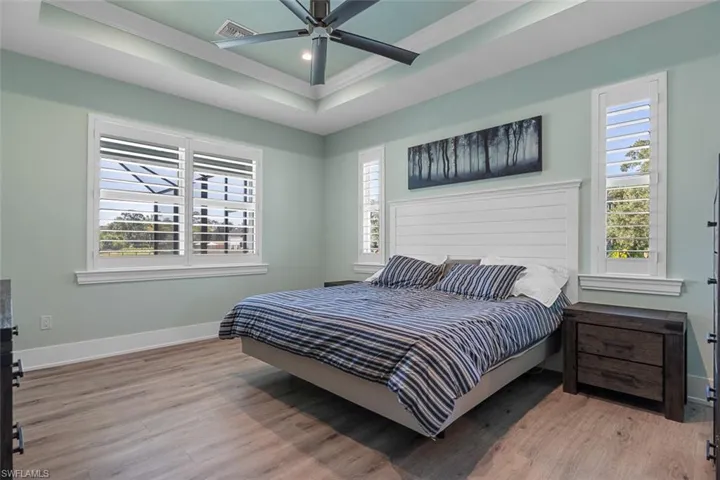 Bedroom with a raised ceiling, light wood-style floors, a ceiling fan, and crown molding