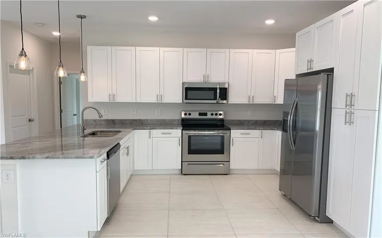 Kitchen featuring appliances with stainless steel finishes, light stone countertops, white cabinets, and kitchen peninsula