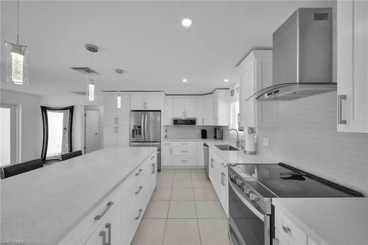 Kitchen featuring appliances with stainless steel finishes, wall chimney range hood, light tile patterned floors, decorative backsplash, and a sink
