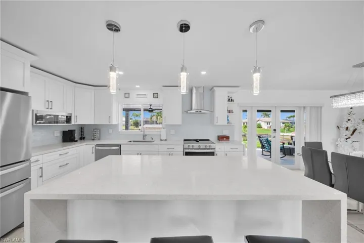 Kitchen with wall chimney exhaust hood, a kitchen bar, decorative backsplash, stainless steel appliances, and a sink
