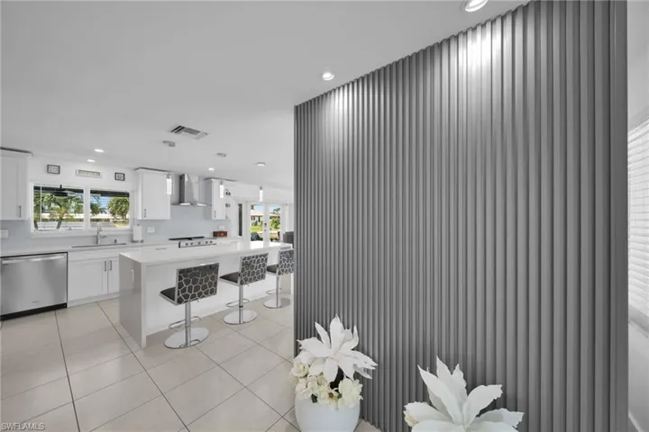 Kitchen with light tile patterned floors, wall chimney exhaust hood, dishwasher, a sink, and light countertops