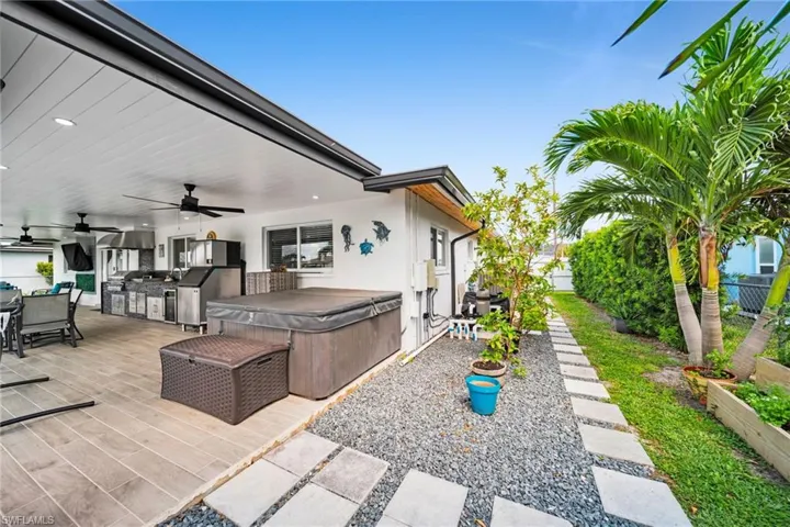 View of patio featuring an outdoor kitchen, a ceiling fan, outdoor dining area, a hot tub, and fence