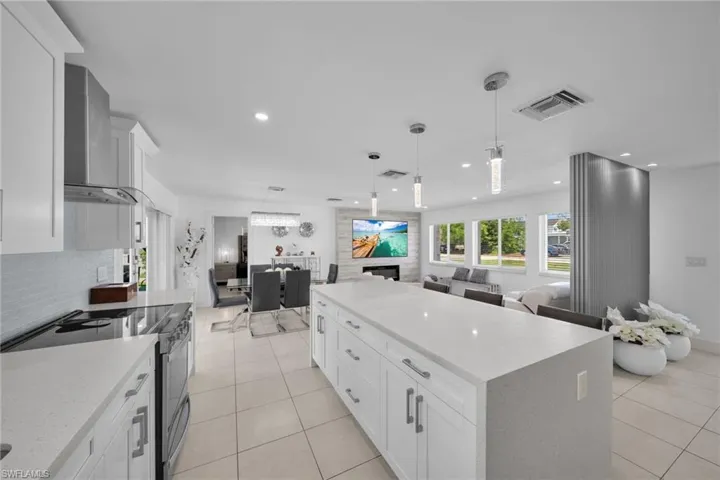Kitchen featuring stainless steel electric range oven, visible vents, wall chimney exhaust hood, open floor plan, and light tile patterned flooring