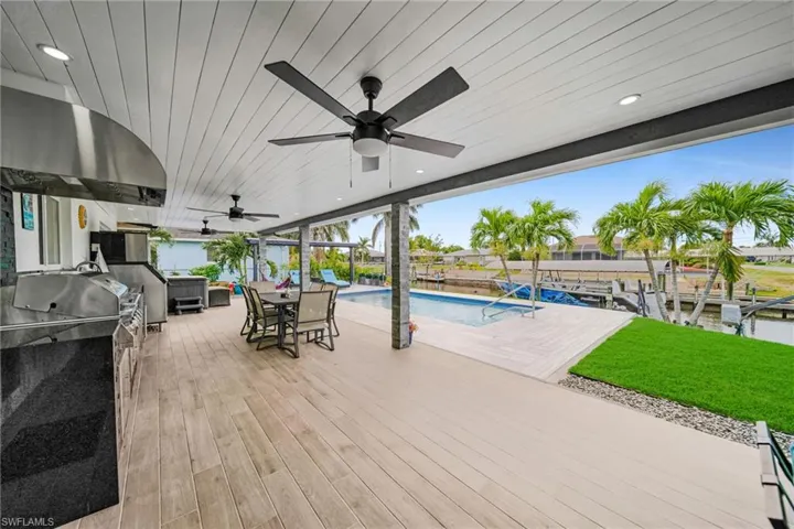 Wooden terrace with a fenced in pool, area for grilling, outdoor dining area, ceiling fan, and a boat dock