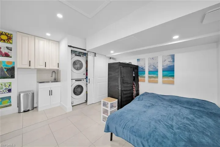 Bedroom with indoor wet bar, a sink, stacked washer / dryer, recessed lighting, and light tile patterned flooring