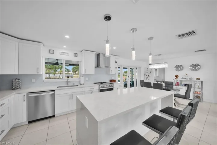 Kitchen with wall chimney exhaust hood, visible vents, a sink, stainless steel appliances, and backsplash