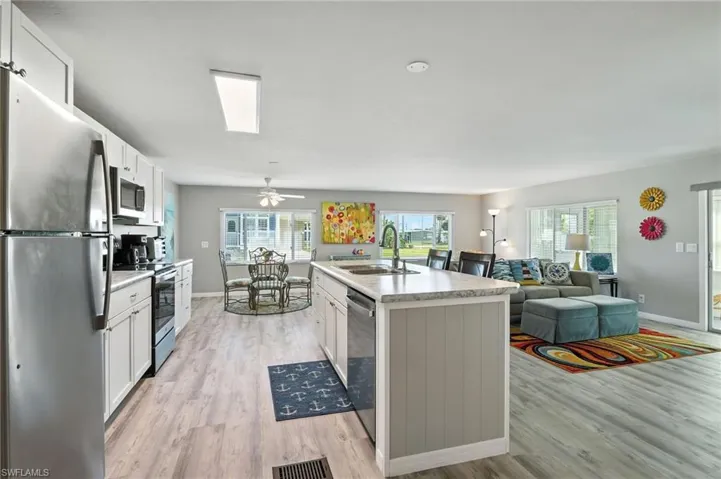 Kitchen featuring stainless steel appliances, light wood finished floors, white cabinetry, light countertops, and a center island with sink