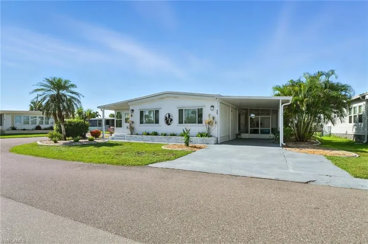 Manufactured / mobile home with 2 driveways, a front lawn, and an attached carport