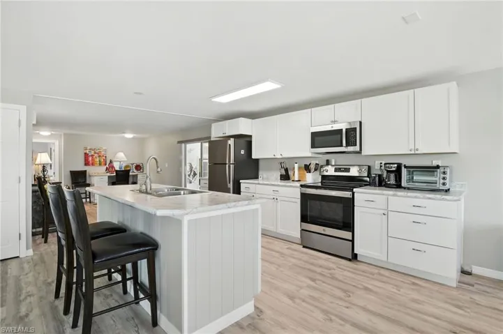 Kitchen featuring stainless steel appliances, a kitchen island with sink, a breakfast bar, white cabinetry, and light wood finished floors