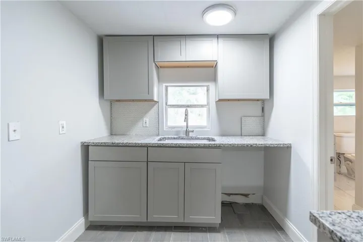 Kitchen featuring gray cabinets, sink, and light stone counters
