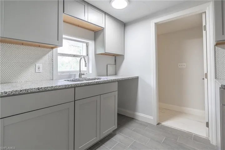 Kitchen featuring light hardwood / wood-style floors, sink, light stone counters, tasteful backsplash, and gray cabinetry