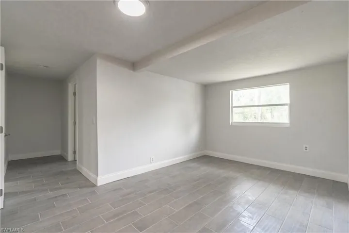 Empty room with light wood-type flooring and beam ceiling