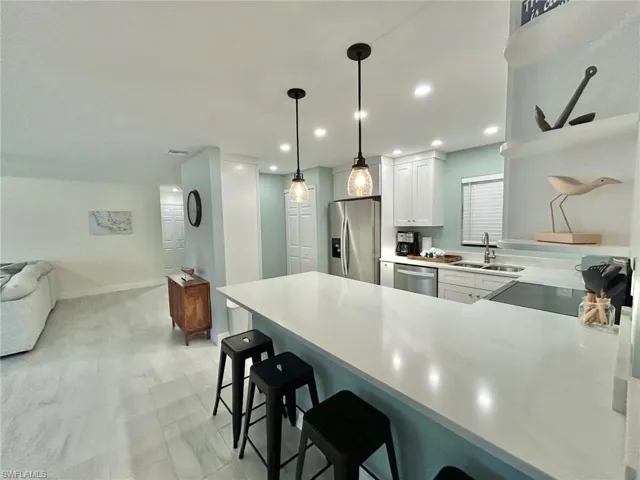 Kitchen featuring a kitchen breakfast bar, a peninsula, stainless steel appliances, white cabinetry, and hanging light fixtures